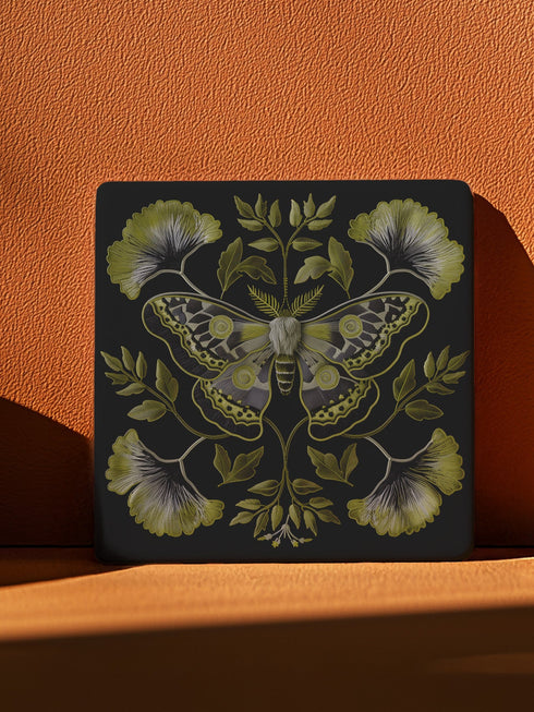 Square black ceramic coaster featuring a detailed chartreuse luna moth illustration surrounded by symmetrical botanical elements including ginkgo-inspired leaves and delicate foliage.